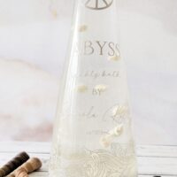 Detailed view of the real white sand and artistic ocean waves on the Salsola Kali Abyss bubble bath bottle.